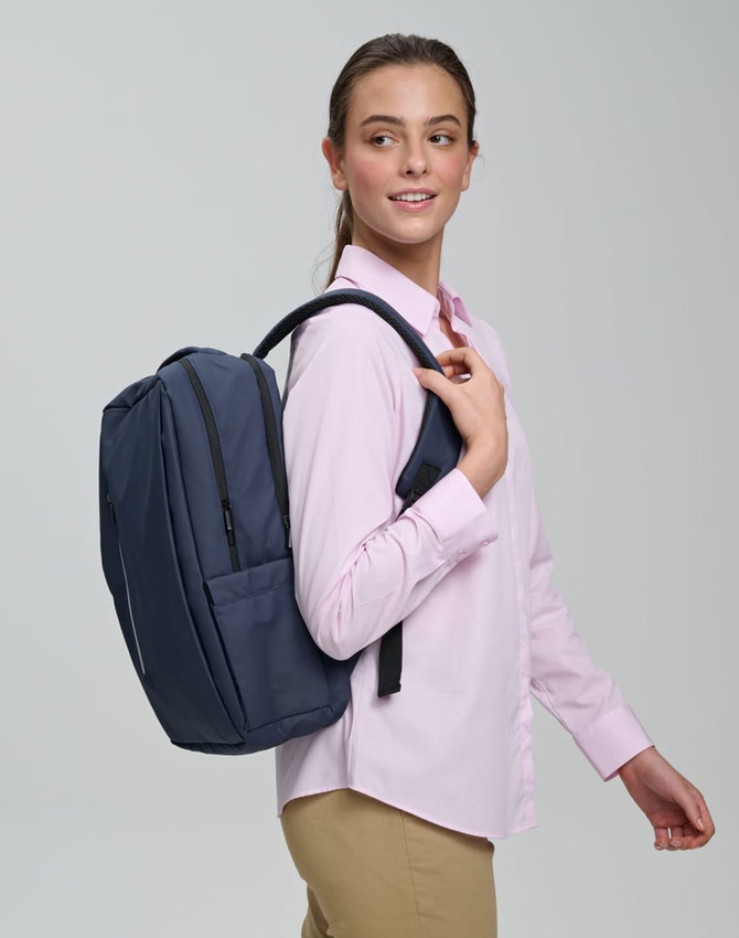 A navy PU backpack is carried on one shoulder by a smiling model wearing a light pink shirt.