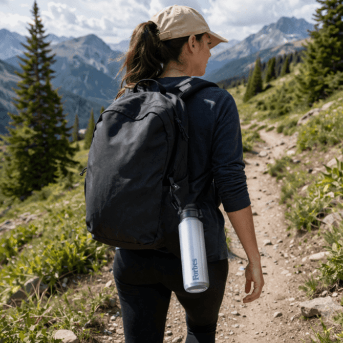 A drink bottle in silver hanging from a backpack, with a mountainous landscape in the background.