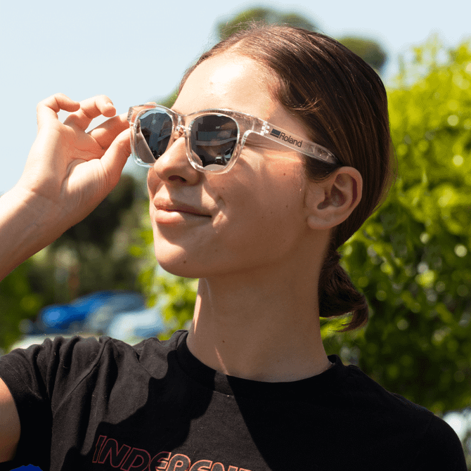A pair of clear and dark grey polarised sunglasses worn by a person with a ponytail, outdoors.