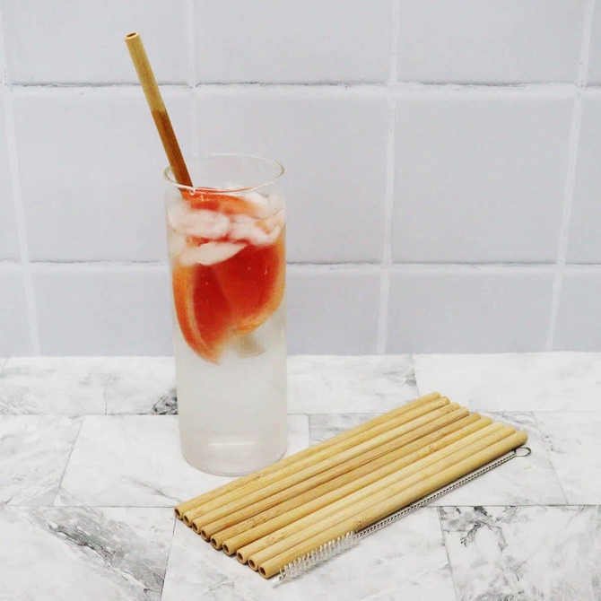 A drink bottle with ice and fruit slices, next to a set of bamboo straws in a light natural colour.
