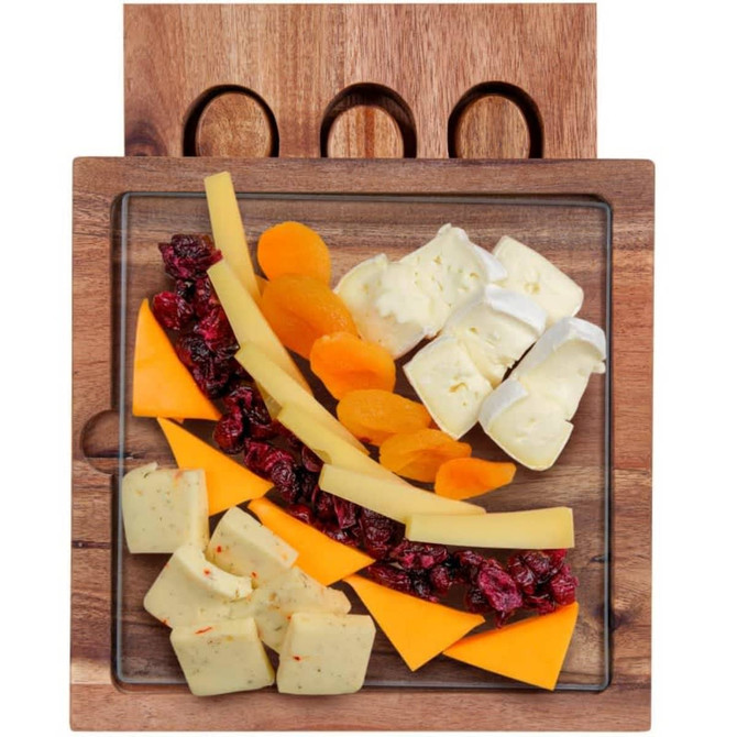 A glass cheese board with various cheeses, dried fruits, and a wooden holder featuring three circular cutouts.