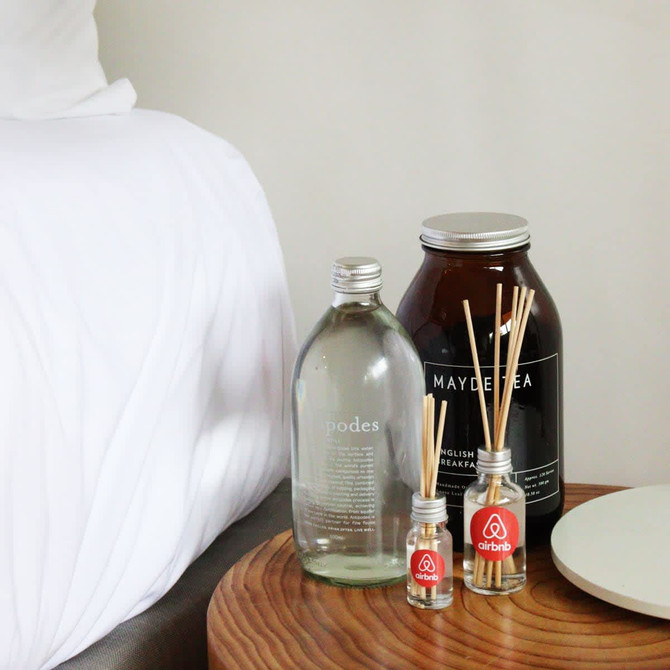A 10ml reed diffuser with several reeds, alongside a drink bottle and a large jar, all on a wooden bedside table.