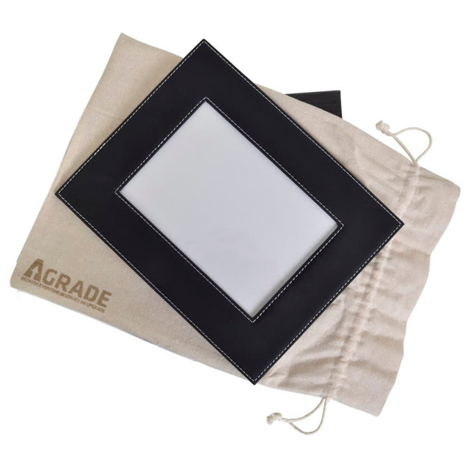 A black 5x7 photo frame with white stitching rests on a beige drawstring bag featuring a logo.