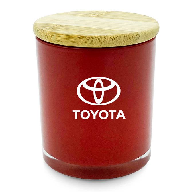 A medium, red candle in a glass jar with a bamboo lid and a logo on the front.