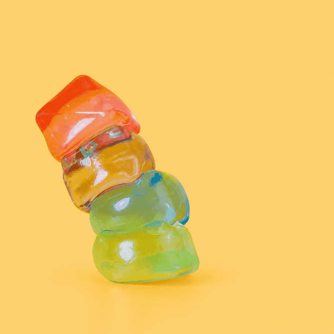 A vibrant stack of jelly cube sensory toys in red, orange, yellow, and green against a bright yellow background.