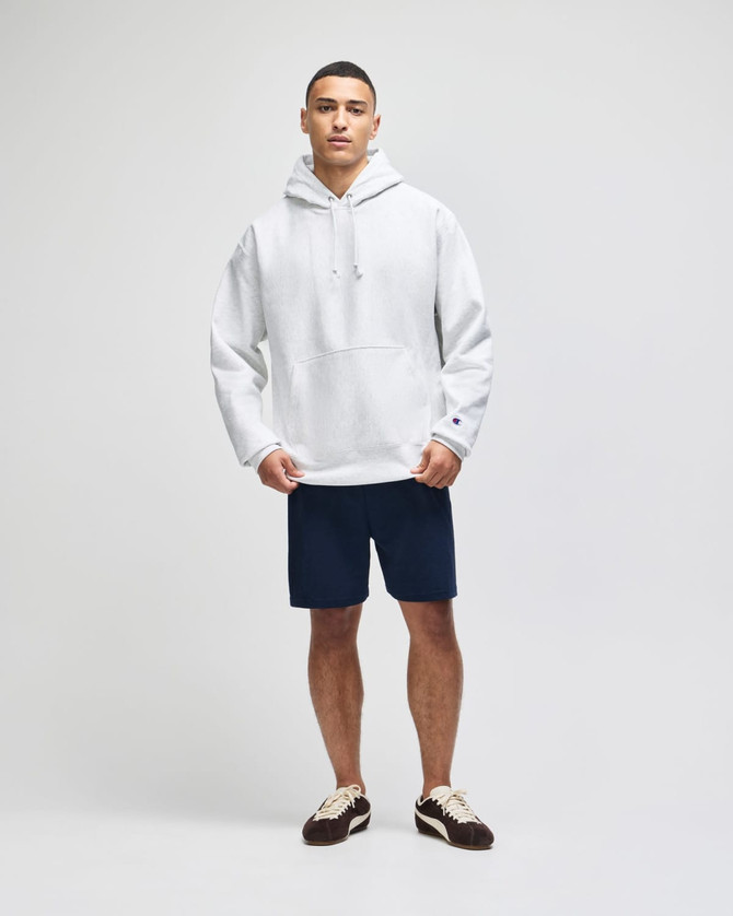 A model wearing a grey Champion Reverse Weave® pullover hooded sweatshirt with navy shorts and brown shoes.