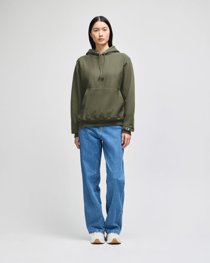 A model wearing an olive green pullover hooded sweatshirt with a logo, paired with blue jeans.