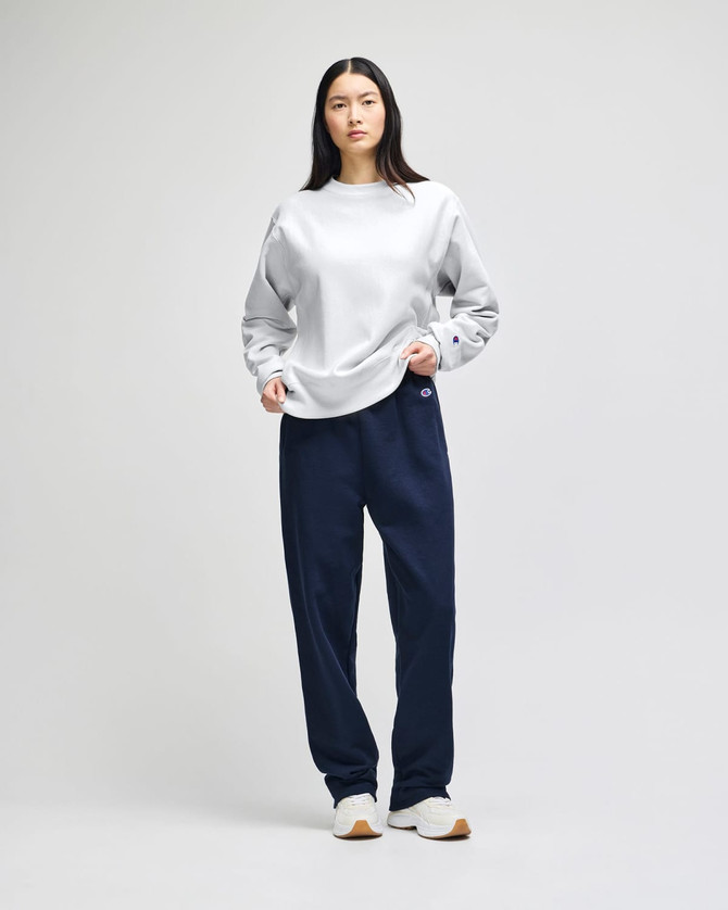 A model wearing a grey Champion Reverse Weave® adult crew sweatshirt and navy pants stands against a neutral background.