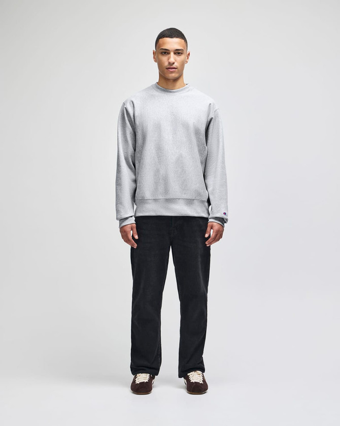 A grey Champion Reverse Weave® adult crew sweatshirt worn by a model, paired with dark trousers and shoes.