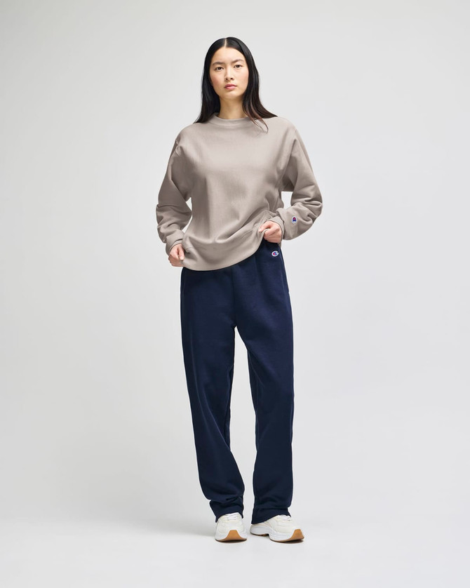 A model wearing a beige Champion Reverse Weave® adult crew sweatshirt and navy trousers, featuring a logo.