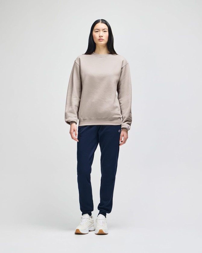 A model wears a beige Champion Powerblend® adult crewneck sweatshirt paired with navy trousers and white sneakers.