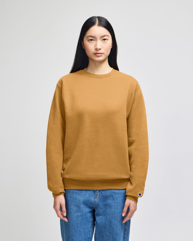 A model wears a mustard-coloured Champion Powerblend® crewneck sweatshirt, paired with blue jeans.