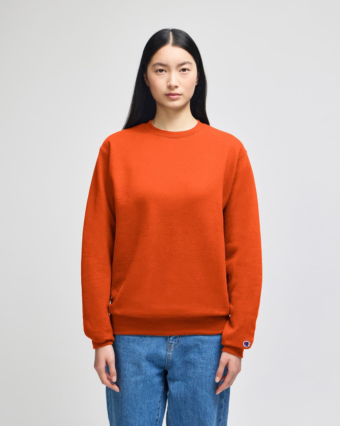 An orange crewneck sweatshirt displayed on a model, featuring a logo on one sleeve.