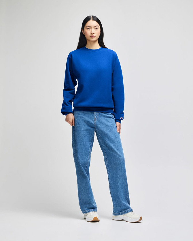 A woman wearing a bright blue crewneck sweatshirt paired with light blue jeans and white sneakers.