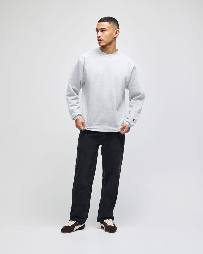 A grey adult crewneck sweatshirt displayed on a model, paired with black trousers and shoes. The sweatshirt features a logo.