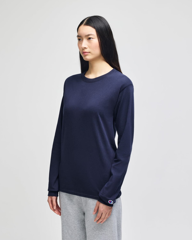 A long-sleeve t-shirt in navy blue with a logo, worn by a model alongside grey pants.