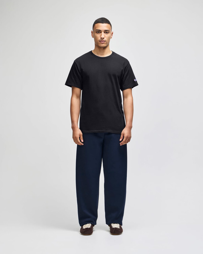 A black short sleeve T-shirt worn with navy blue pants, featuring a logo on the T-shirt.