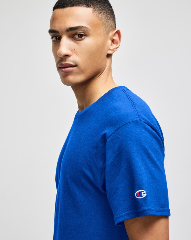 A blue Champion adult jersey short sleeve t-shirt, featuring a logo on the sleeve and a model in profile.