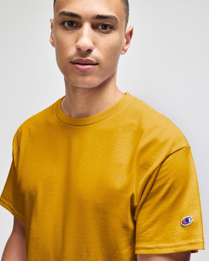 A mustard yellow Champion adult jersey short sleeve T-shirt with a logo on the sleeve.