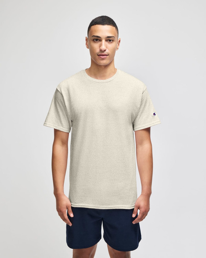 A light beige short sleeve t-shirt worn by a model, featuring a logo on the sleeve. Paired with navy shorts.