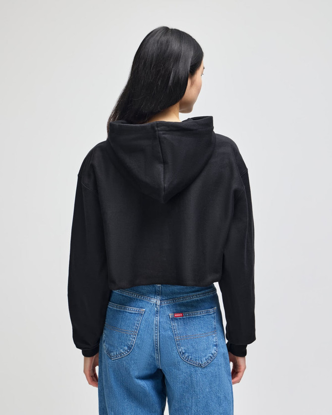 A black cropped hoodie with a hood, worn by a person facing away, paired with blue jeans.