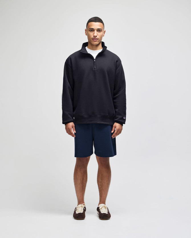A model wearing a black Champion Powerblend® quarter-zip pullover and navy shorts, standing against a plain background.