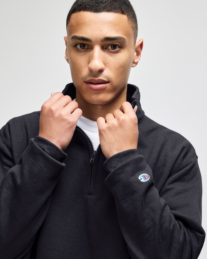 A man in a black quarter-zip pullover with a logo on the sleeve, posing against a neutral background.