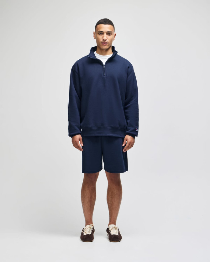 A navy quarter-zip pullover and matching shorts, featuring a logo, displayed on a model standing against a plain background.