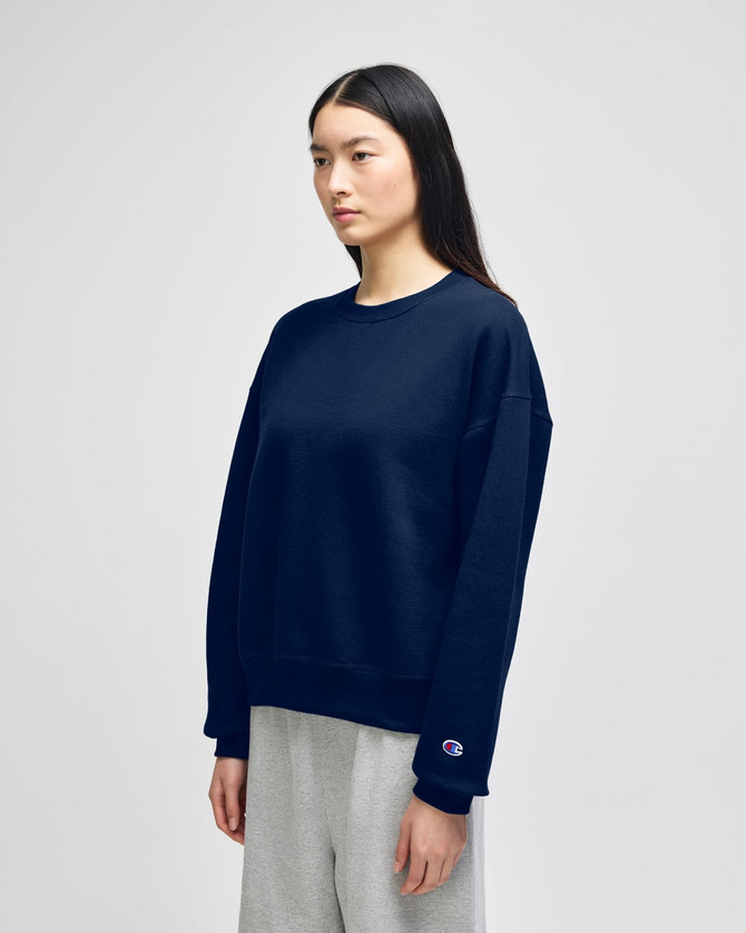 A woman wearing a navy blue Champion Powerblend® crewneck sweatshirt paired with grey bottoms, featuring a logo.