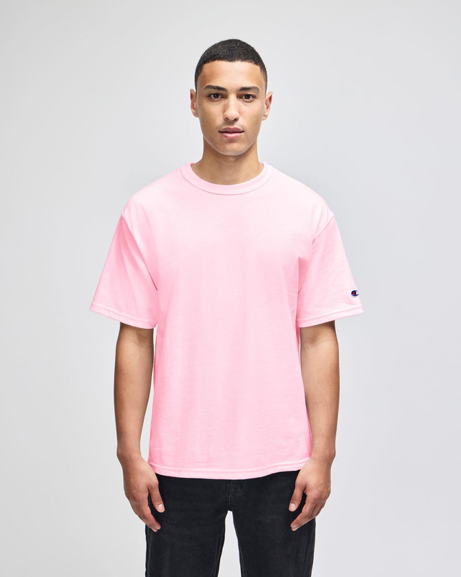 A pink Champion Adult Heritage Jersey T-Shirt displayed on a male model, featuring a logo on the sleeve.