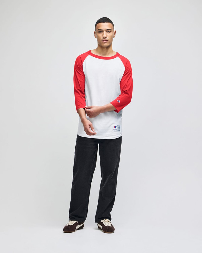 A model wearing a white and red raglan baseball T-shirt with three-quarter sleeves, paired with dark pants.