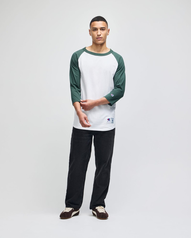 A raglan baseball T-shirt in white with green sleeves, paired with black pants. It features a logo on the hem.