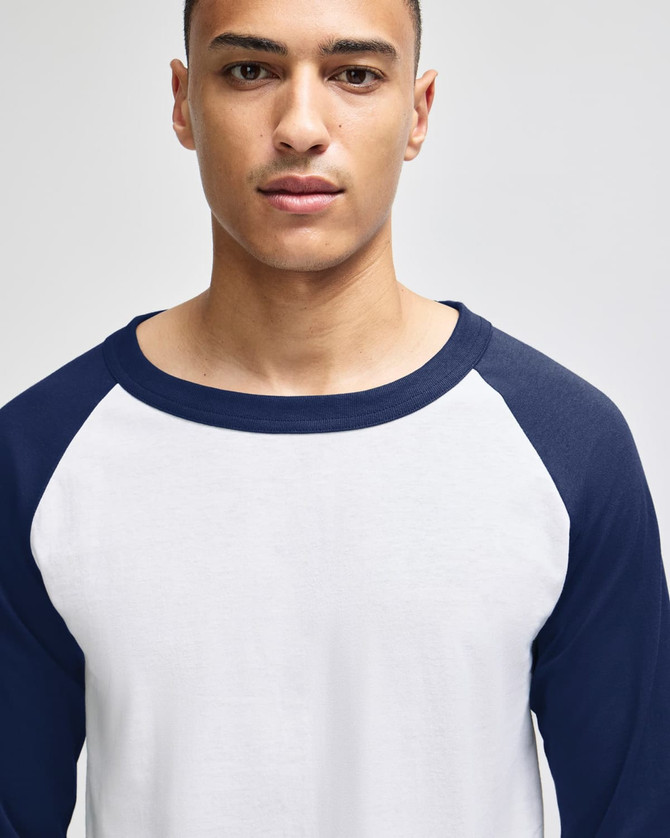 A white and navy raglan baseball T-shirt for adults, featuring long sleeves and a crew neck. It has a logo.