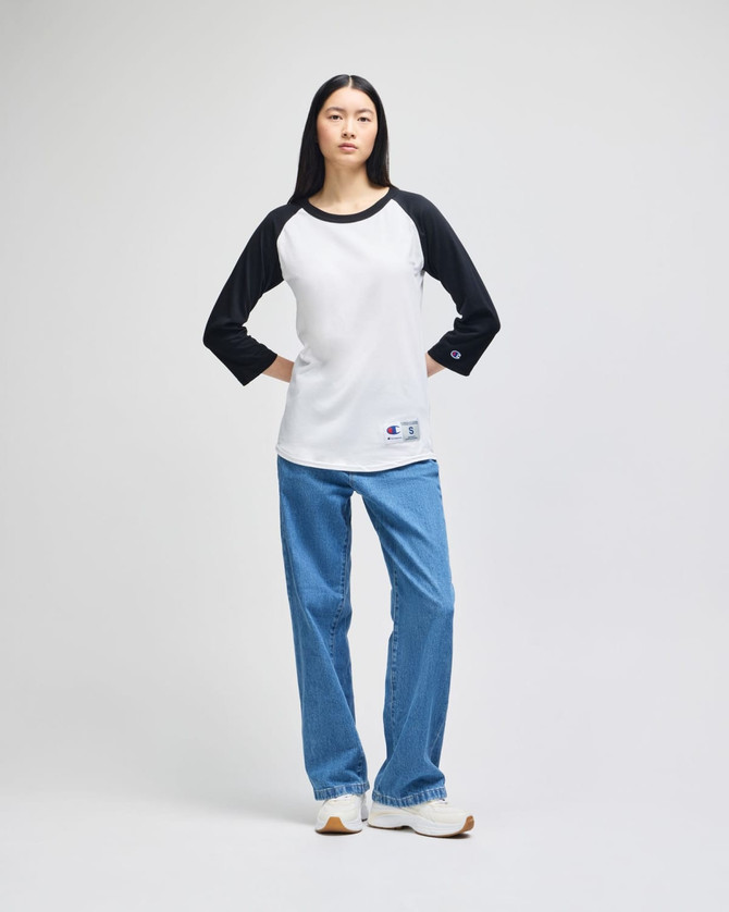 A black and white raglan baseball t-shirt paired with blue jeans, worn by a model standing against a neutral background.