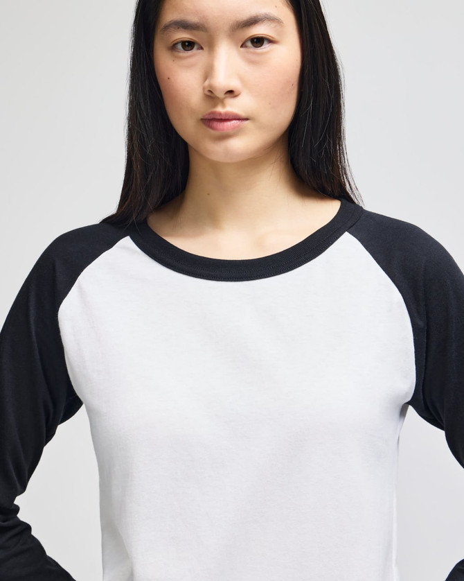 A long-sleeve raglan baseball t-shirt featuring white body and black sleeves. It has a logo on the front.