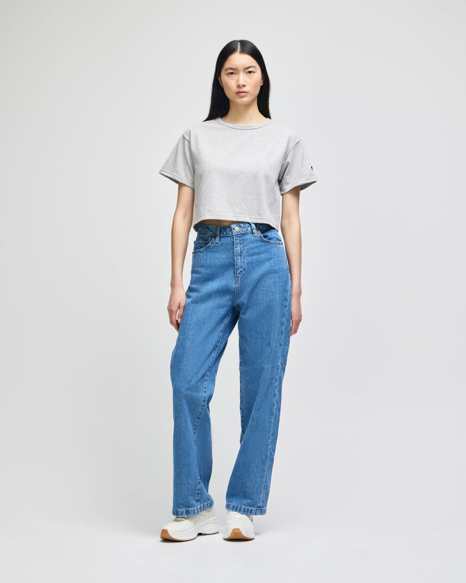 A grey cropped short sleeve t-shirt paired with blue jeans, worn by a model against a plain background.