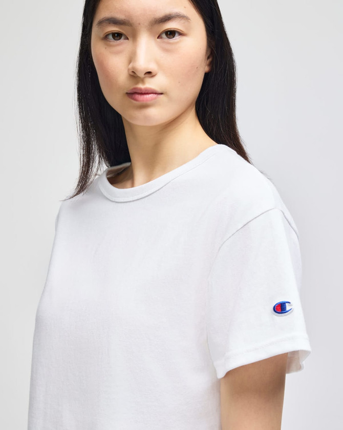 A white cropped short sleeve t-shirt featuring a logo on the sleeve.