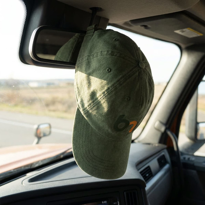 A green vintage washed cap hanging from the mirror inside a vehicle, with a logo on the front.