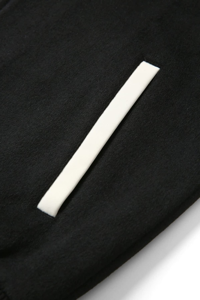 A close-up of a black wool blend soft shell varsity jacket featuring a white pocket detail and a logo.