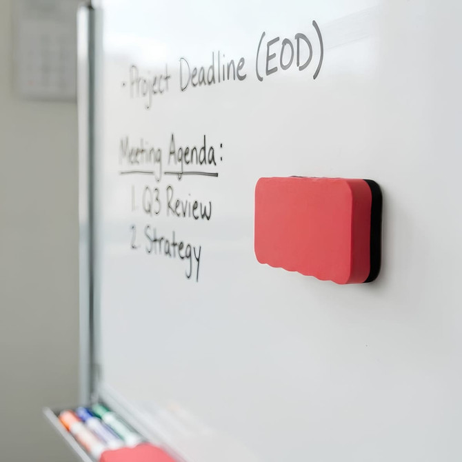 A magnetic foam whiteboard eraser in red and black, positioned on a whiteboard beside written notes.