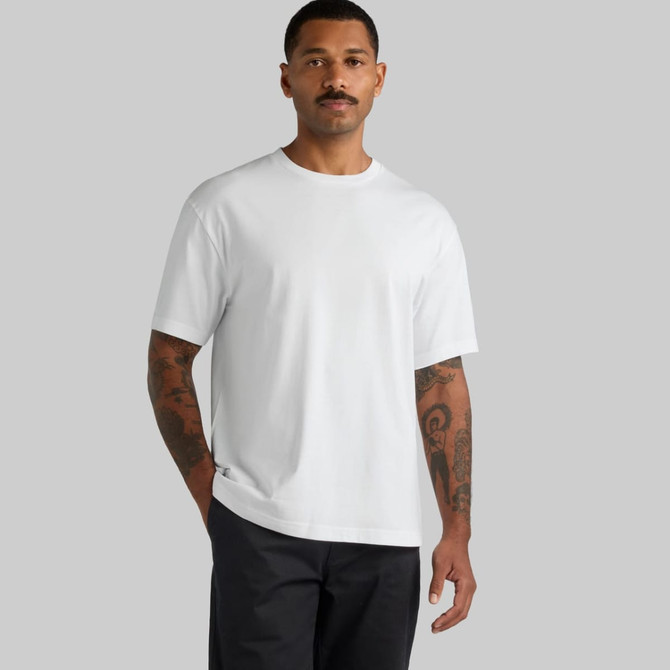 A white block tee featuring a relaxed fit, worn by a model with tattoos in a neutral background.