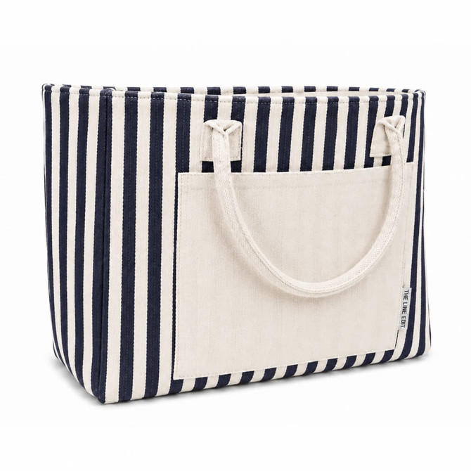 A striped tote bag featuring navy and white stripes with a solid cream front pocket and two handles.