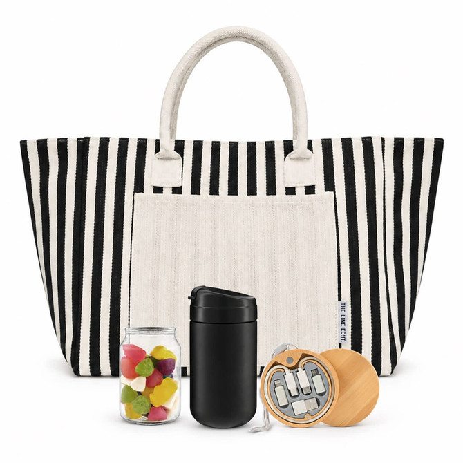 A striped tote bag with a white pocket, containing a black drink bottle, a jar of colourful sweets, and a wooden keychain.
