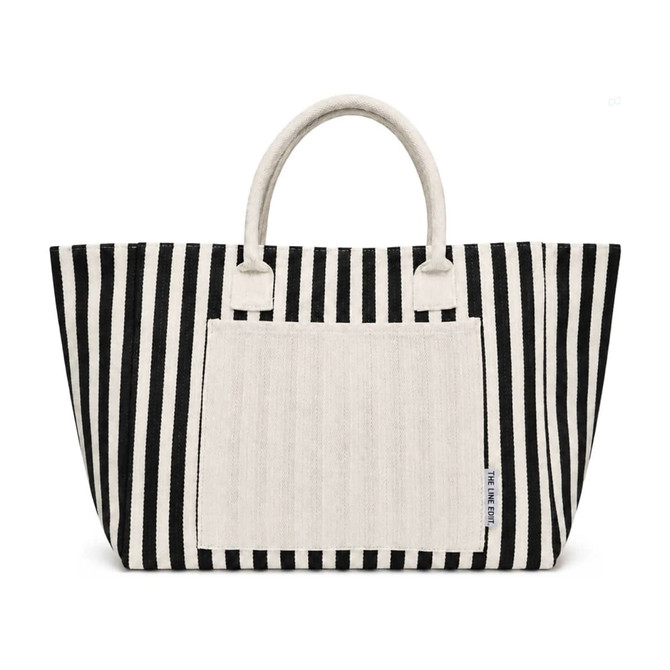 A striped tote bag in black and white with a plain cream-coloured front pocket and handles. It has a logo.