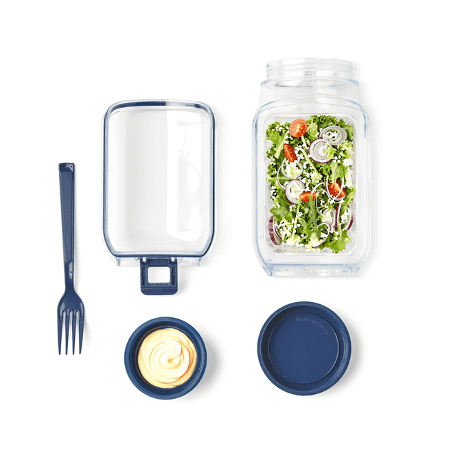 A salad jar with a blue lid, containing salad, a fork, and a separate container with dressing.