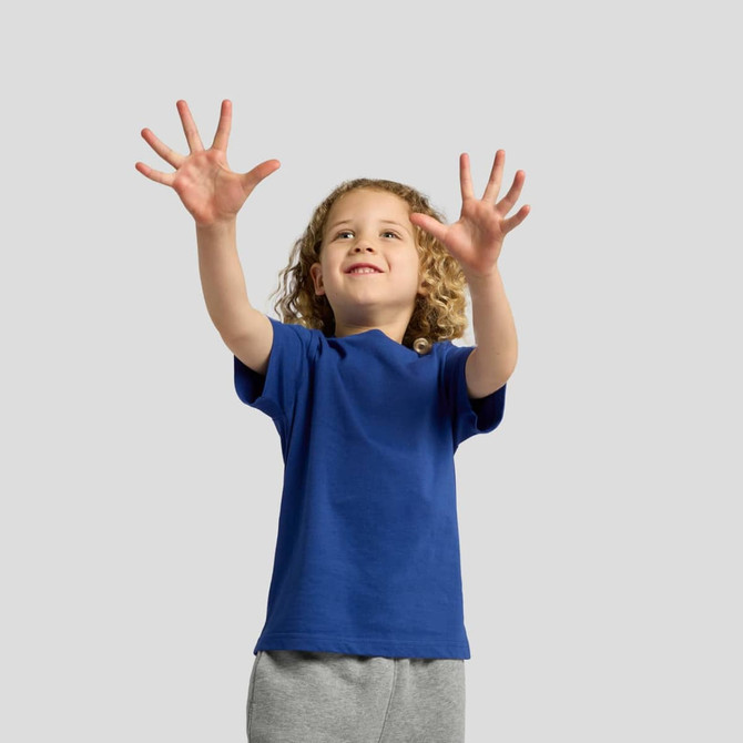 A child in a blue t-shirt reaches out with both hands, smiling. The background is plain and grey.