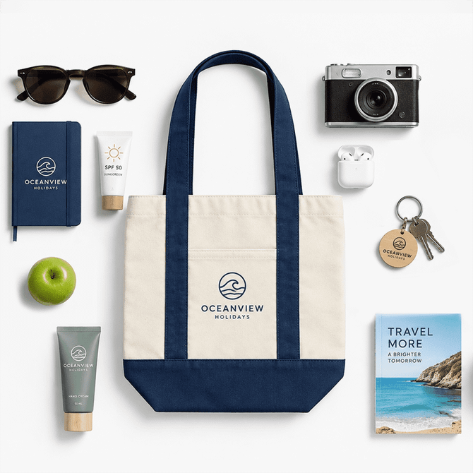 A mini canvas tote in navy and cream, surrounded by sunglasses, a camera, skincare products, and a notebook.