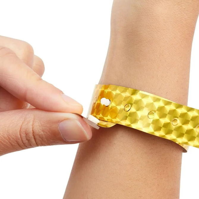 A hand adjusts a holographic yellow wristband with a textured pattern, featuring a small logo.