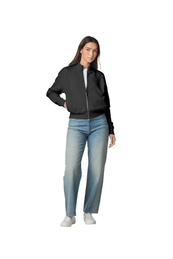 A woman wearing a black full-zip jacket and blue jeans, standing with one hand on her hip. The jacket has a logo.