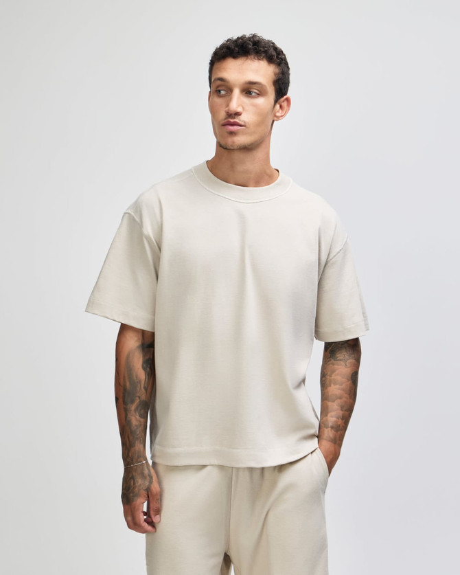 A unisex heavyweight cotton boxy t-shirt in a light beige colour, worn by a model with tattoos.